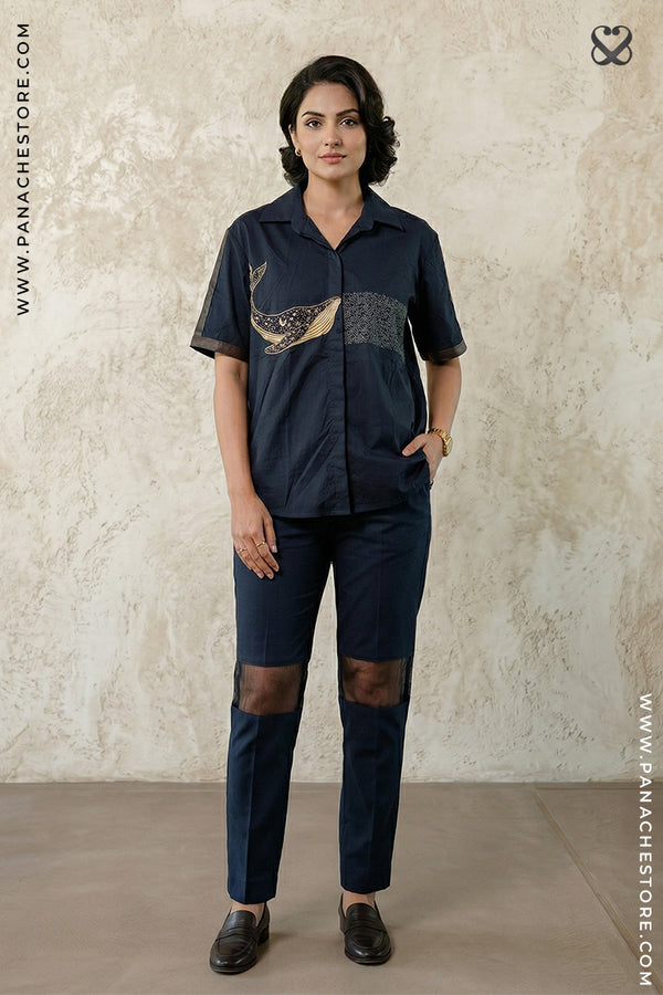 Woman wearing a navy blue outfit with a decorative element, standing against a beige wall.