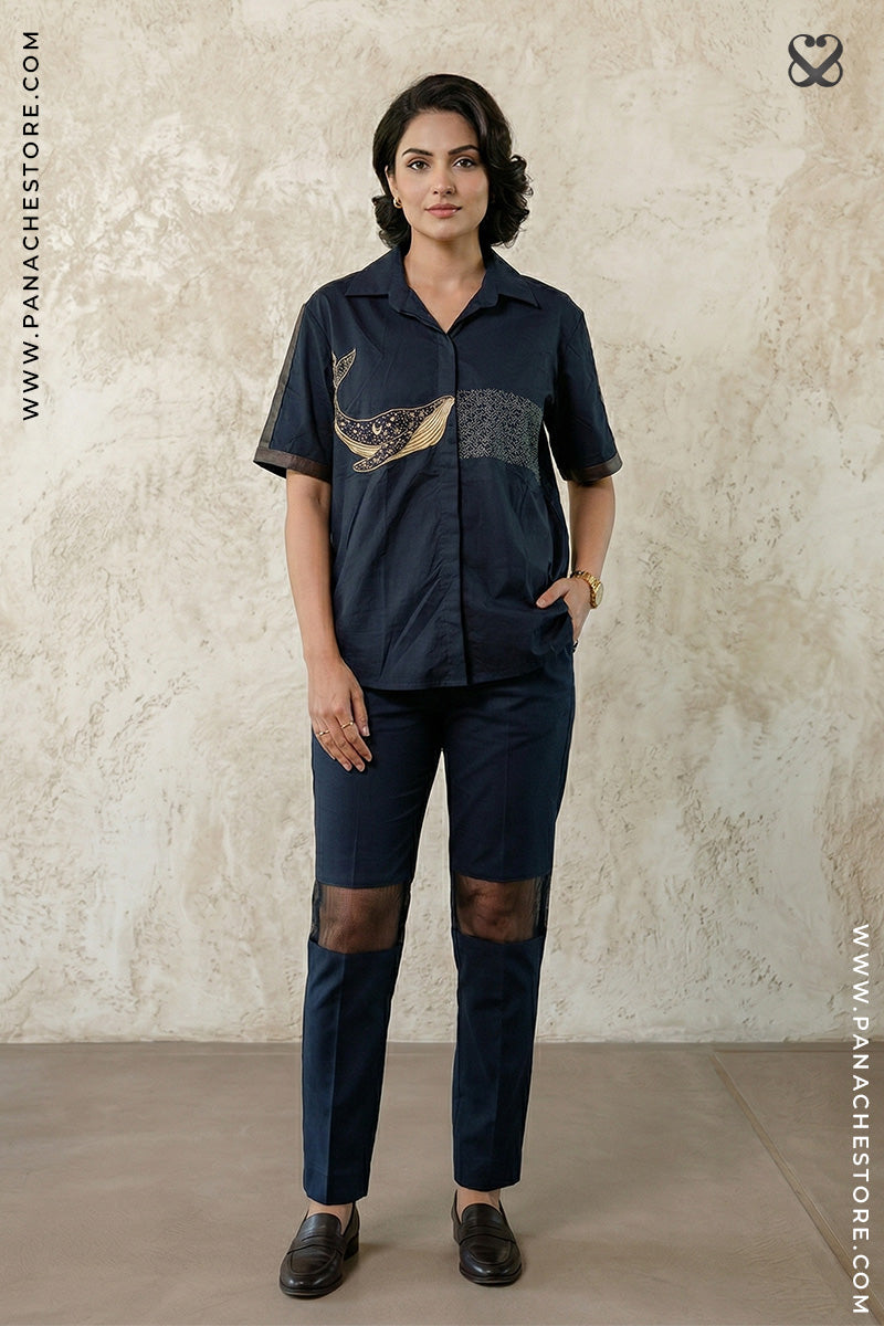 Woman wearing a navy blue outfit with a decorative element, standing against a beige wall.