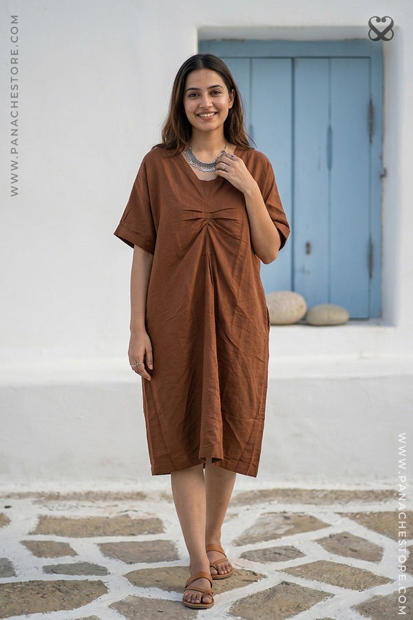 Woman wearing a brown dress standing on a stone pavement with a blue door in the background.