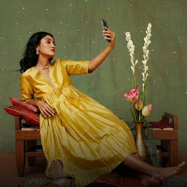 Woman in a yellow dress taking a selfie in a room with flowers and furniture, haldi ceremoney.