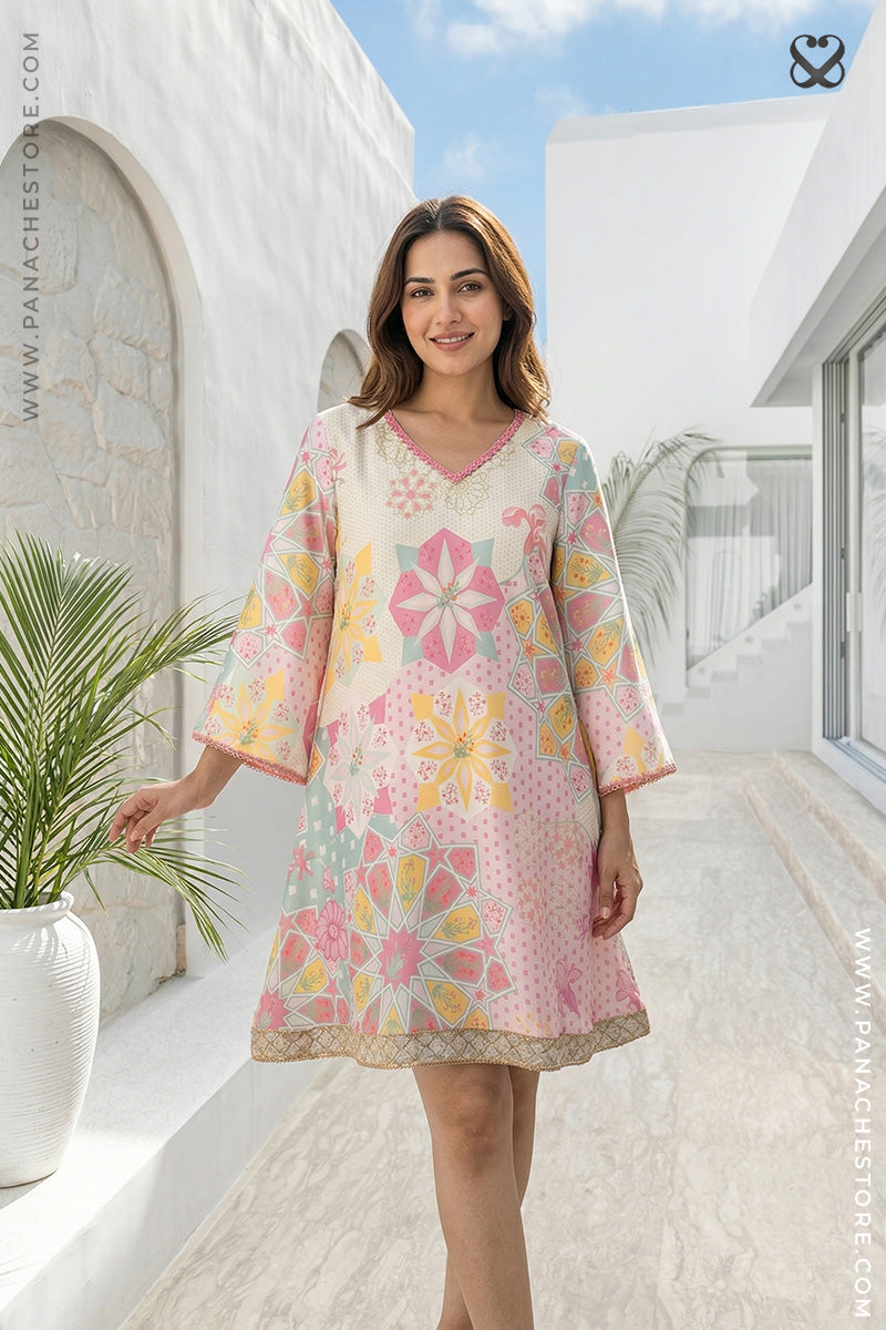 Woman wearing a floral dress standing in a sunlit outdoor setting with white architecture.