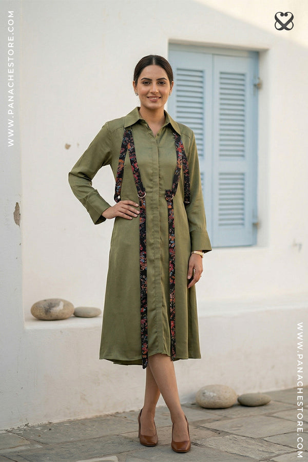 Woman wearing a green dress with suspenders standing in front of a white wall.